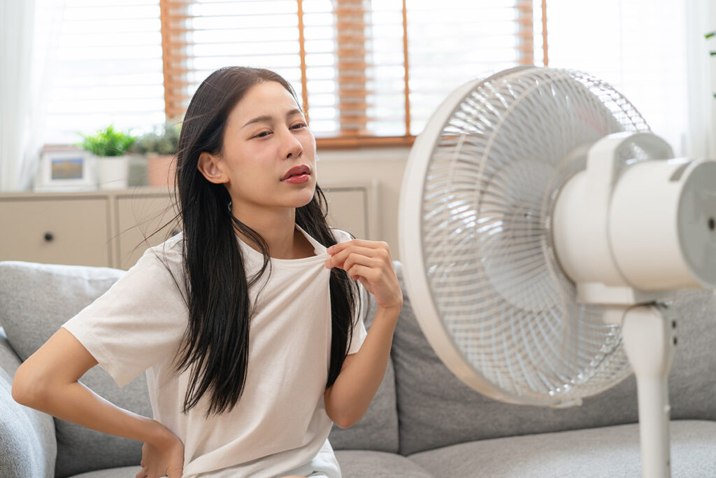 扇風機の前で涼もうとする女性
